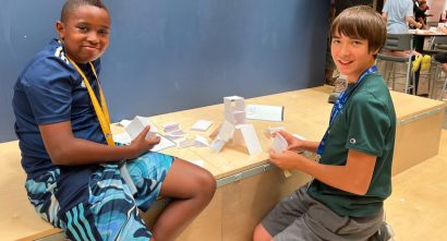 2 CSA learners sitting and smiling in front of the paper team working projects they made