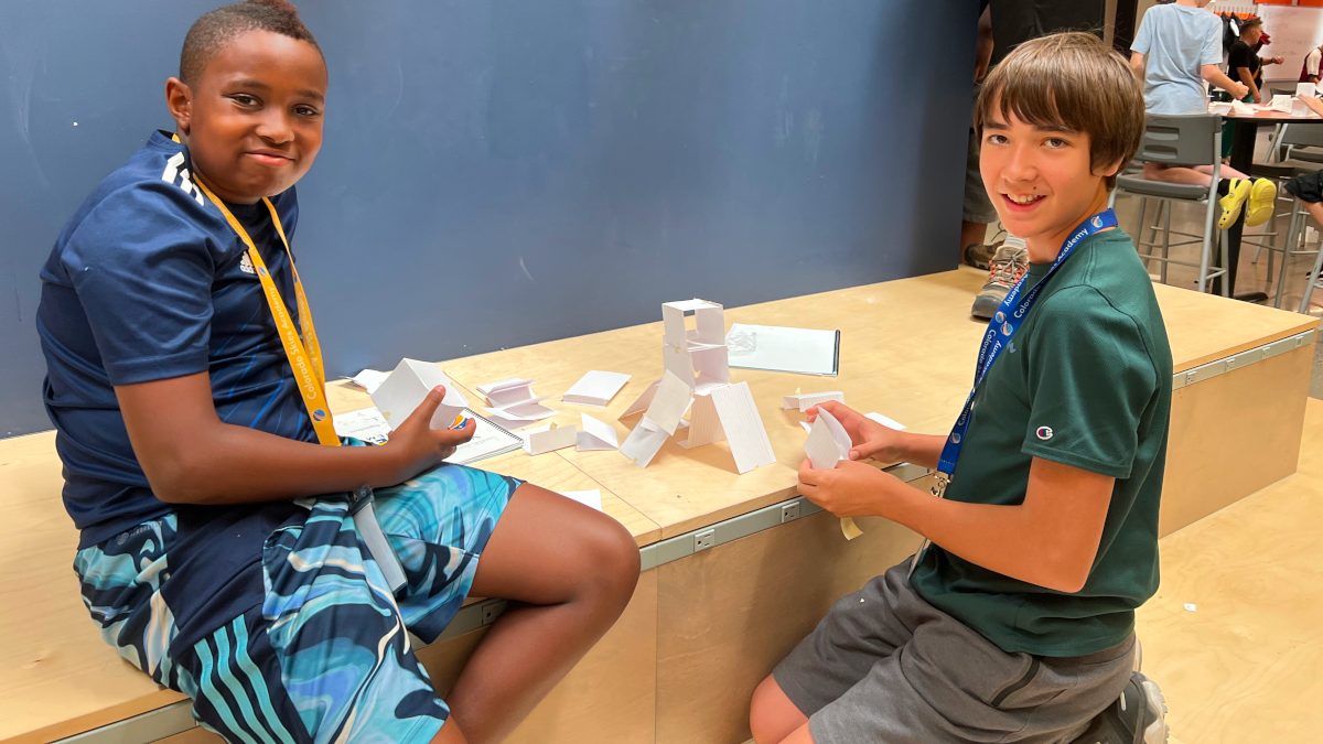 2 CSA learners sitting and smiling in front of the paper team working projects they made